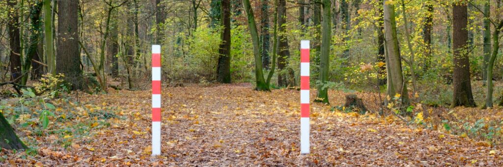 Zwei rot-weiße Absperrpfosten markieren einen Waldweg, um unerlaubte Durchfahrten zu verhindern und die Natur zu schützen. Ideal zur Abgrenzung von geschützten Bereichen.